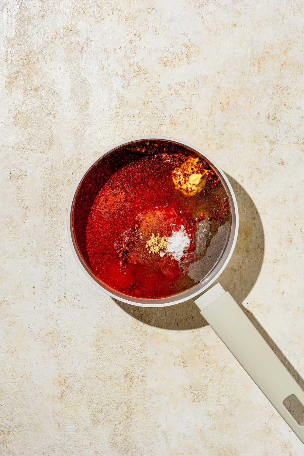 A small pot with ingredients to make Carolina BBQ sauce. The cup is on a tan counter.
