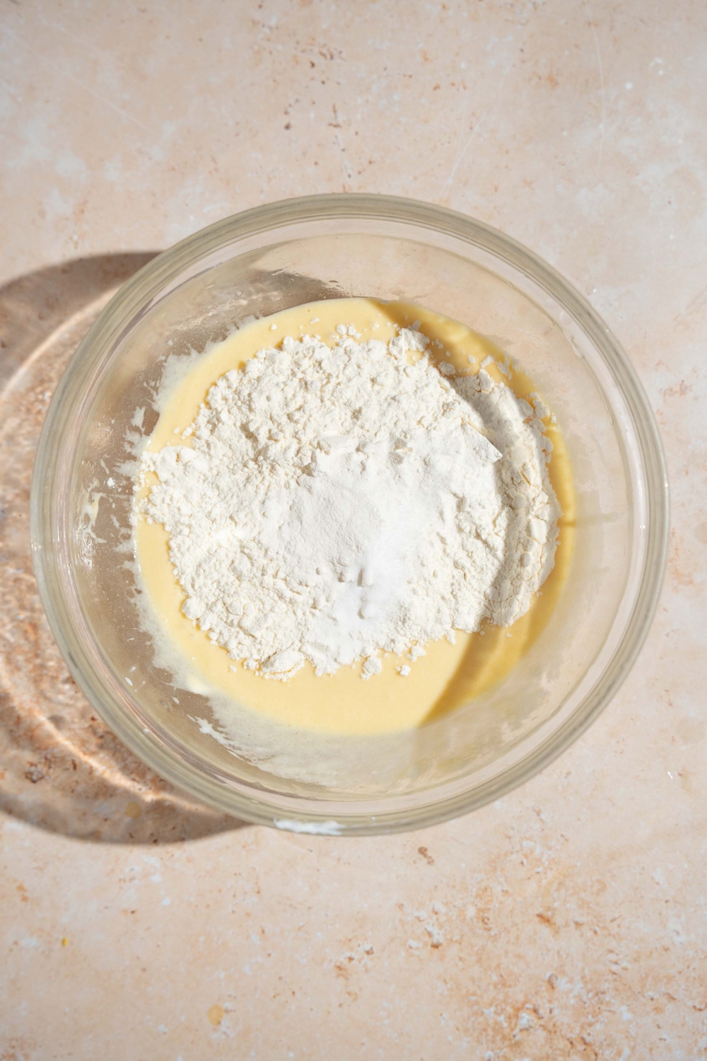 A glass bowl with dry ingredients on top of wet ingredient mixture to make copycat Little Bites muffins. The bowl is on a tan counter.