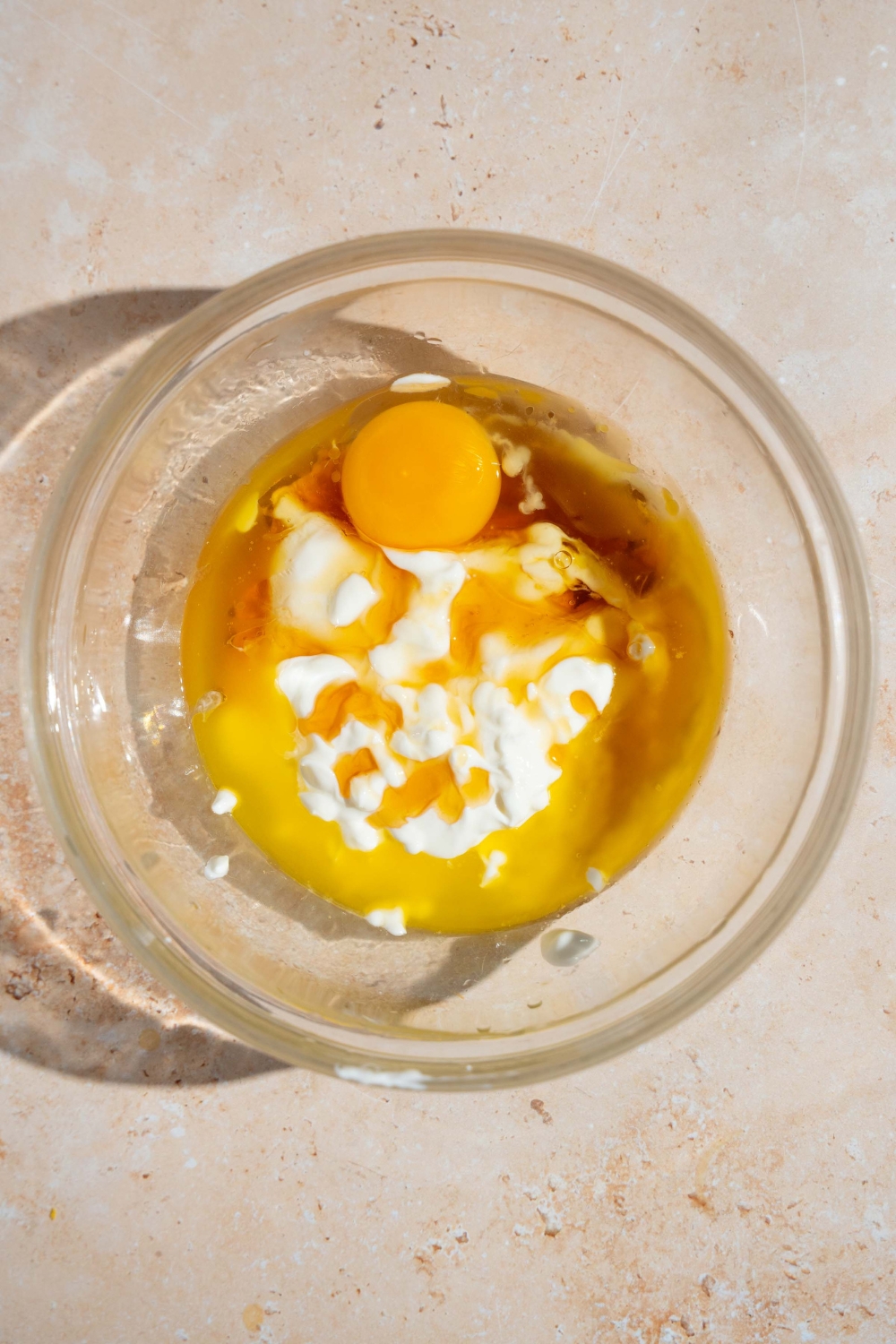 A glass bowl with wet ingredients to make copycat Little Bites muffins including eggs, yogurt, vanilla, and butter. The bowl is on a tan counter.