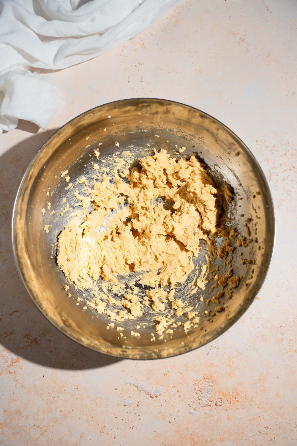 A mixing bowl with a creamed butter mixture. The bowl is on a tan counter with a white cloth napkin.