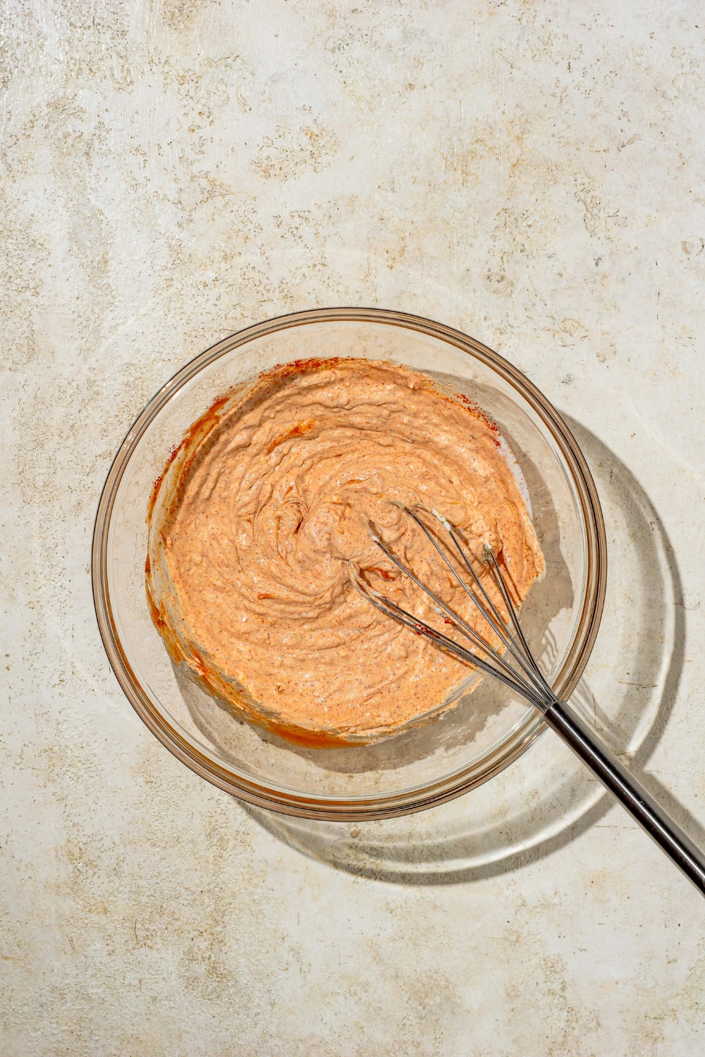 A glass bowl with a whisk mixing ingredients to make copycat Outback bloomin onion sauce.