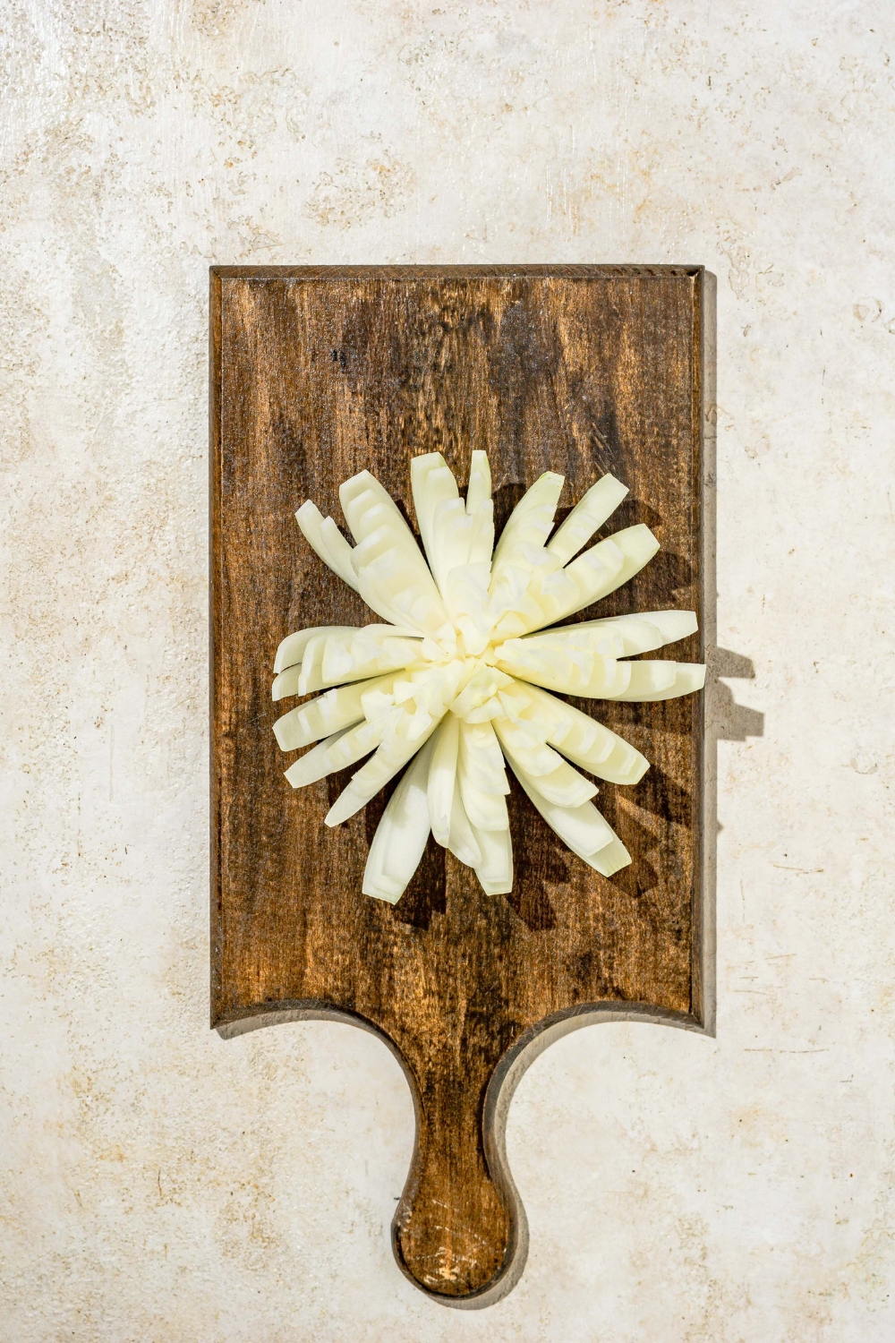 A wooden cutting board with a bloomed onion. The board is on a tan counter.