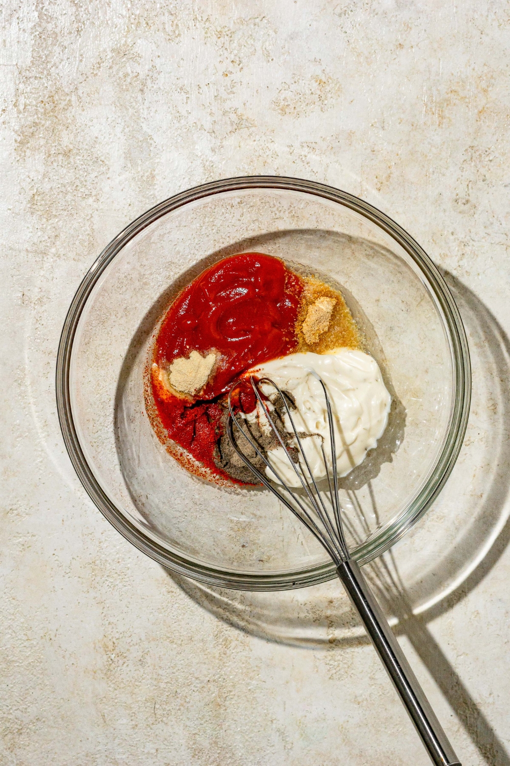 A glass bowl with a whisk mixing ingredients to make copycat Zaxby's sauce. The bowl is on a tan counter.