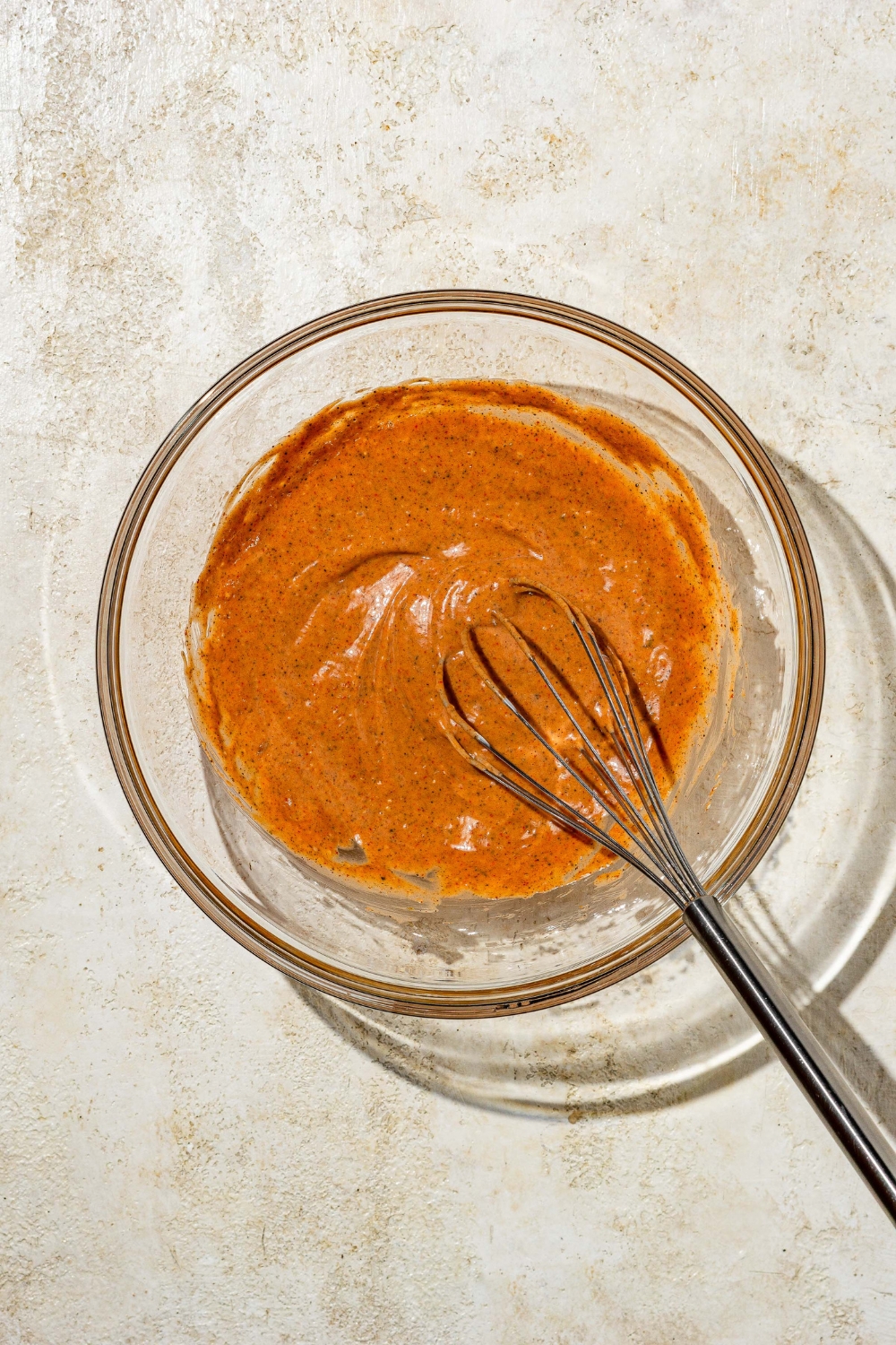 A glass bowl with a whisk mixing copycat Zaxby's sauce. The bowl is on a tan counter.
