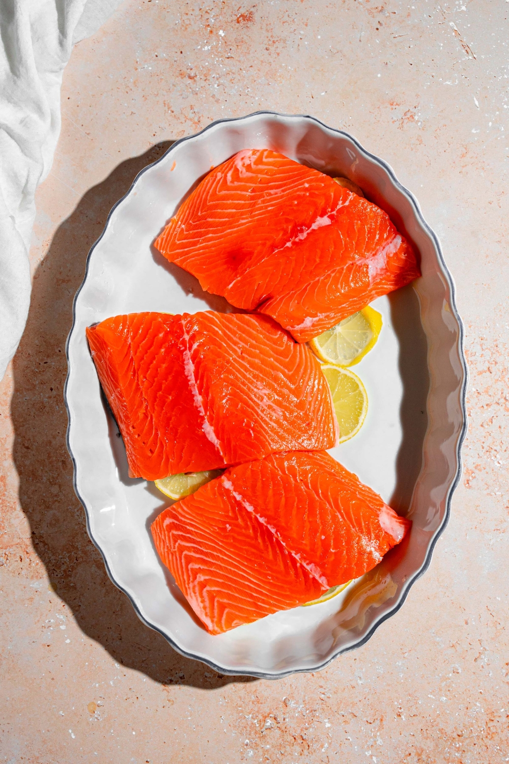A baking dish lined with sliced lemon with Sockeye salmon fillets on top. The dish is on a tan counter.