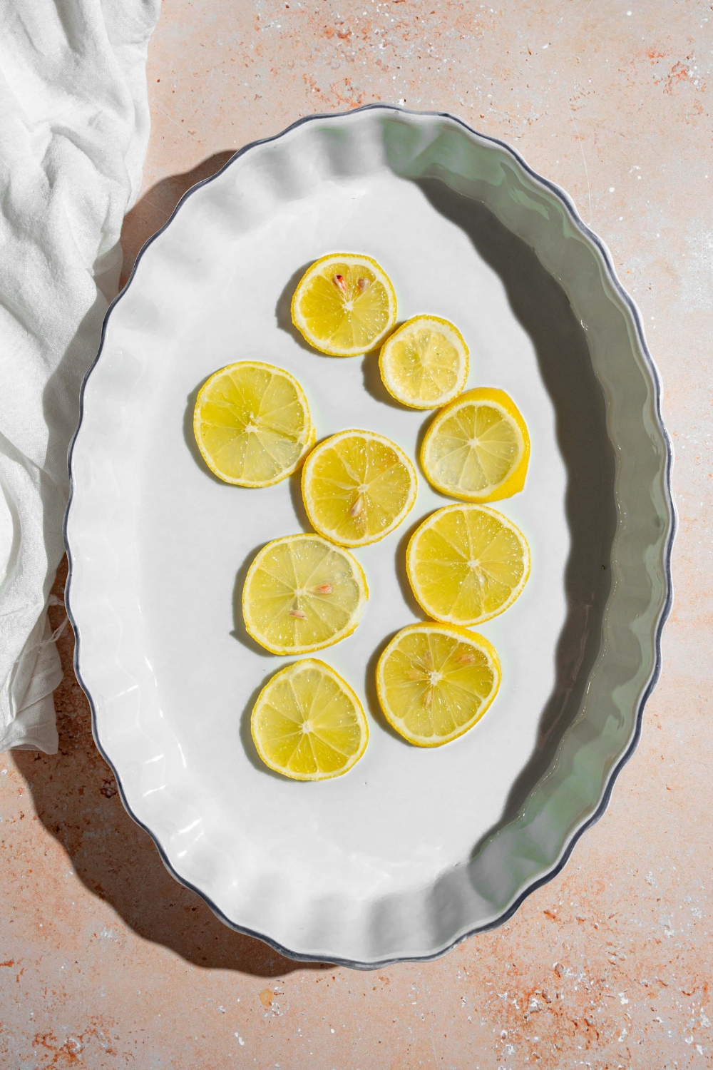 A baking dish with sliced lemon. The dish is on a tan counter with a white cloth napkin.
