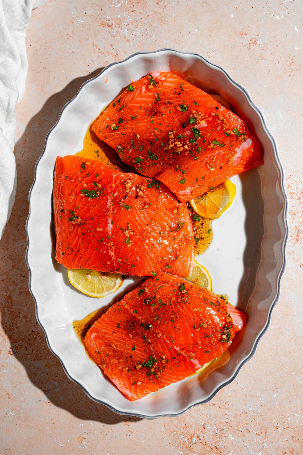 A baking dish with sliced lemon and marinated Sockeye salmon fillets on top. The dish is on a tan counter.