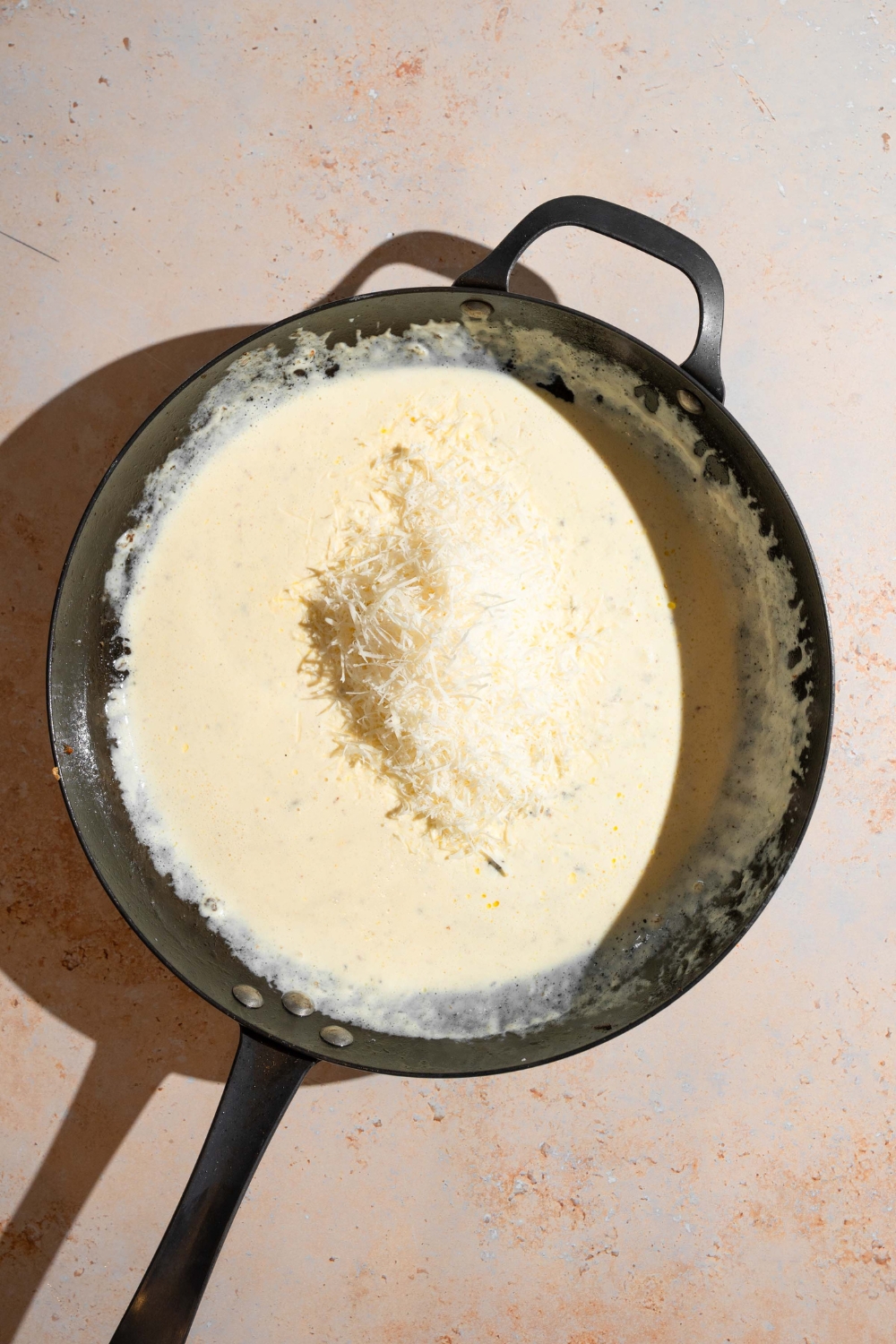 A skillet with a butter, cream, and parmesan mixture. The skillet is on a tan counter.