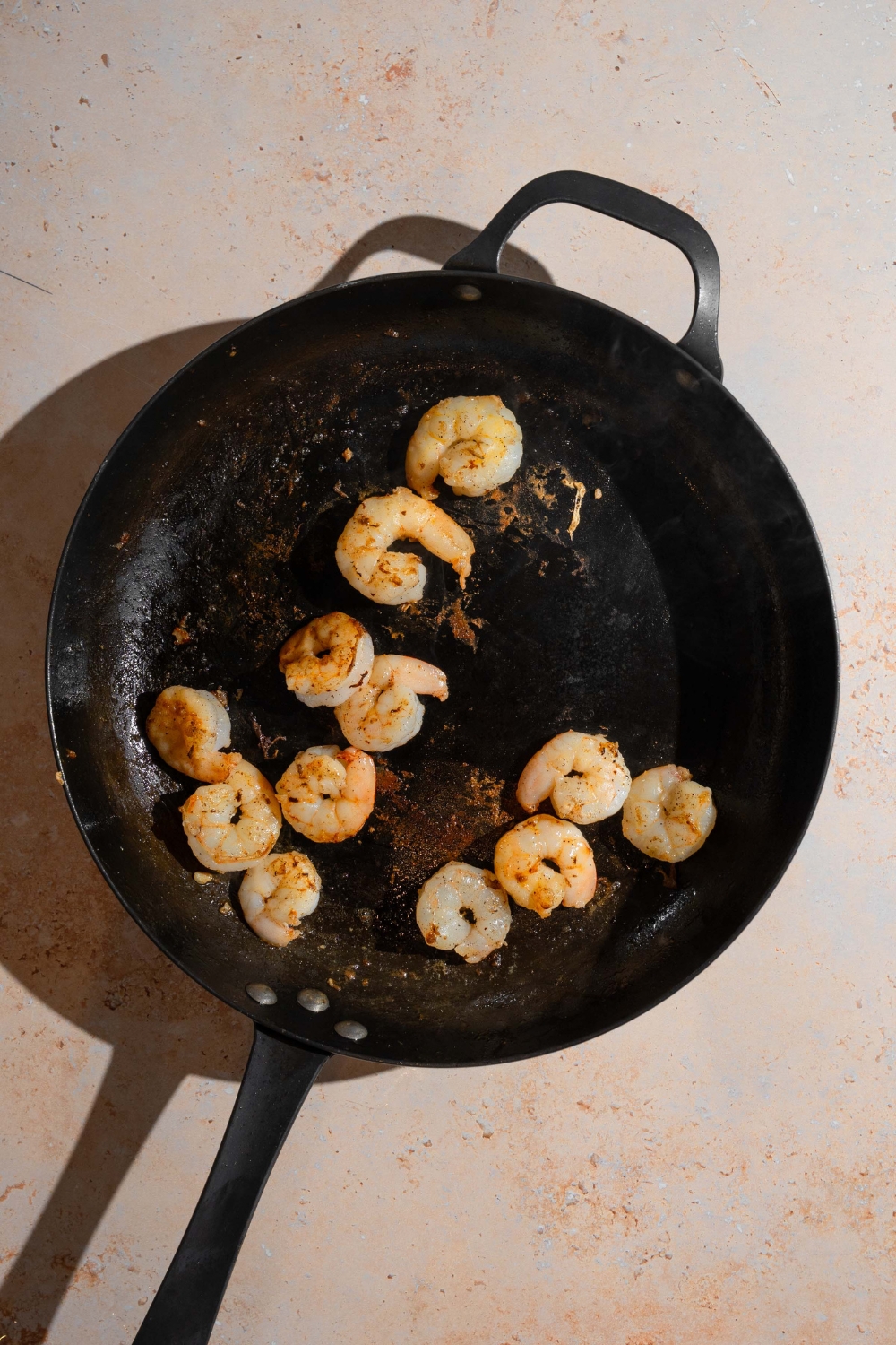 A skillet with shrimp sautéed with oil. The skillet is on a tan counter.