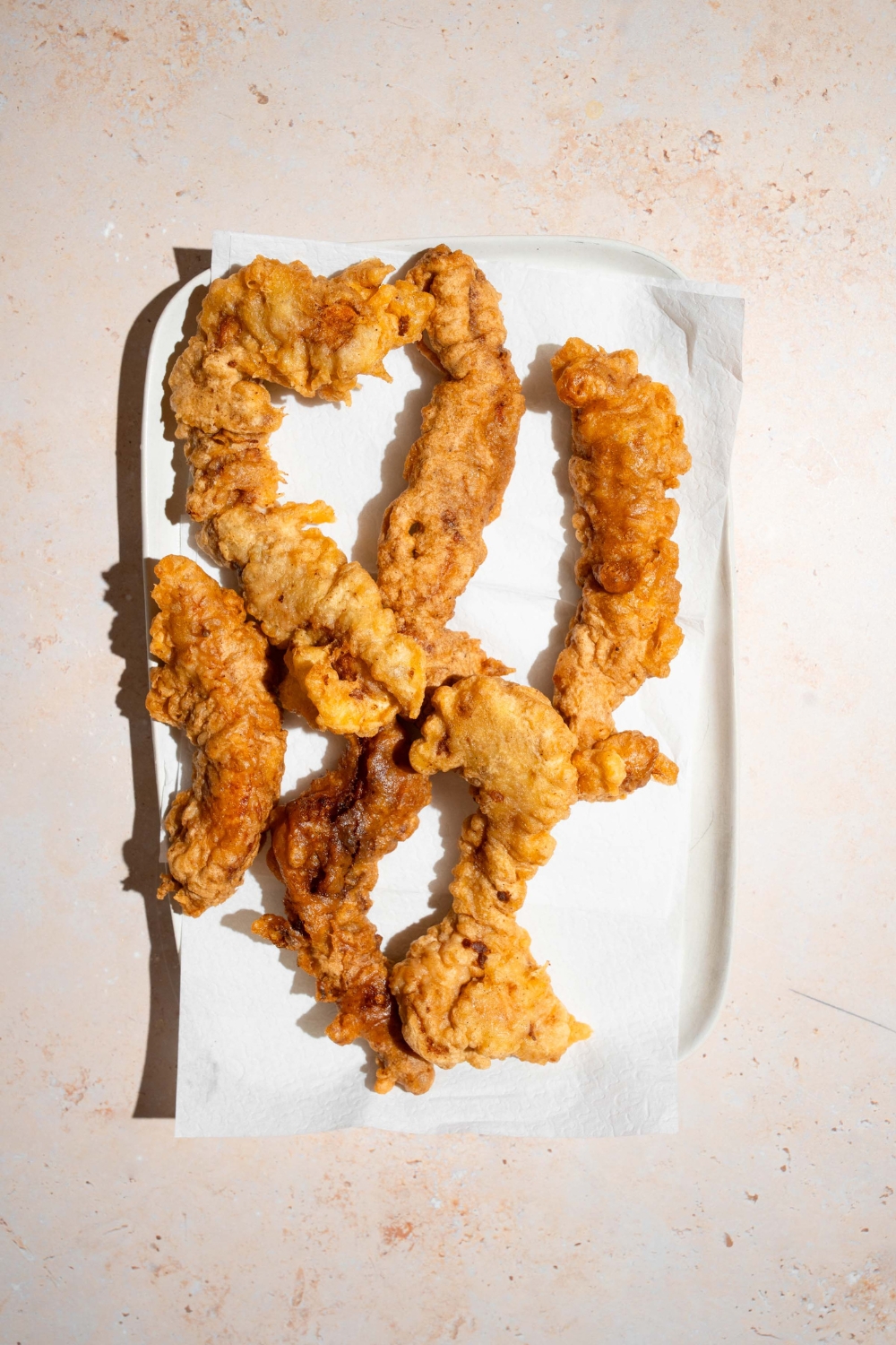 A platter lined with paper towel with fried chicken tempura. The platter is on a tan counter.