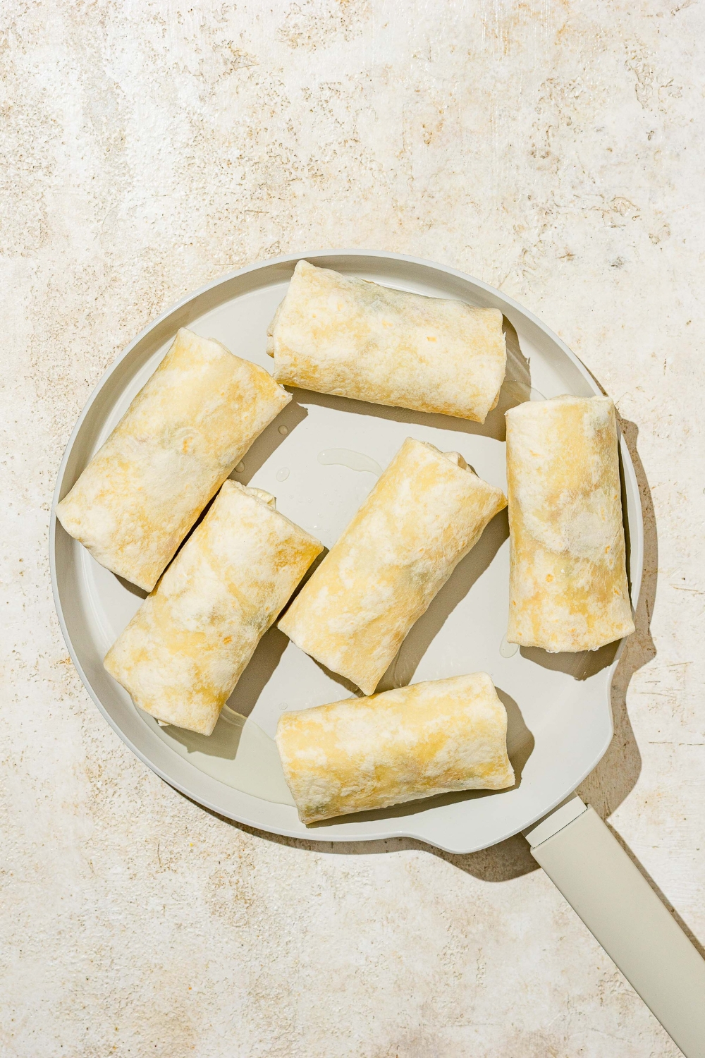 A skillet with wrapped Southwestern egg rolls. The skillet is on a tan counter.