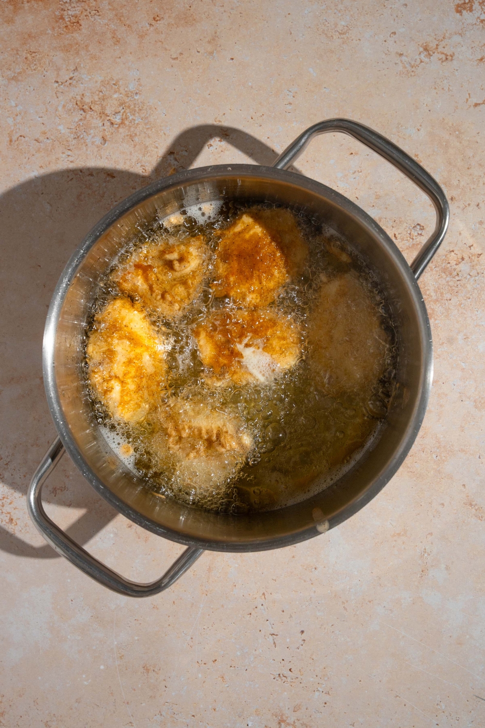 A stock pot of breaded homemade Chick Fil A nuggets frying in oil. The pot is on a tan counter.