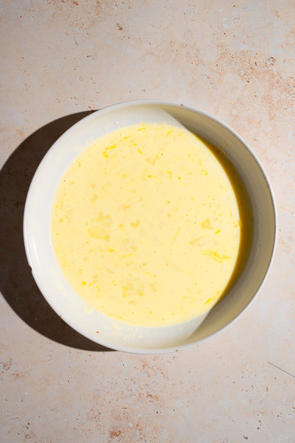 A white bowl of an egg batter. The bowl is on a tan counter.