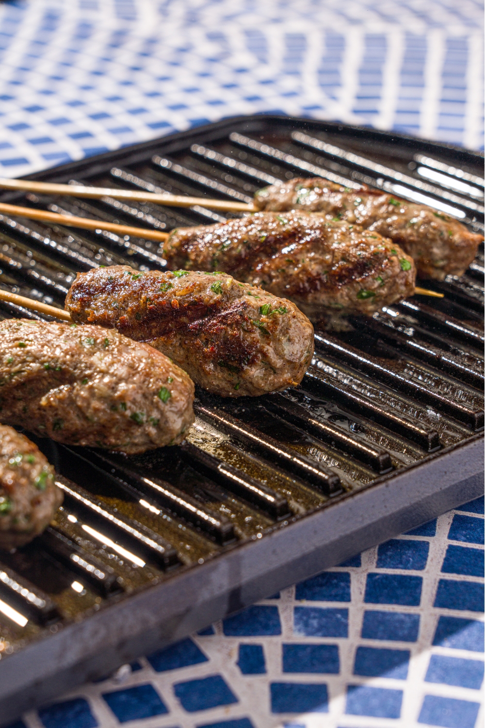 An indoor grill with several Kafta kabobs grilling. The grill is on a tiled counter.