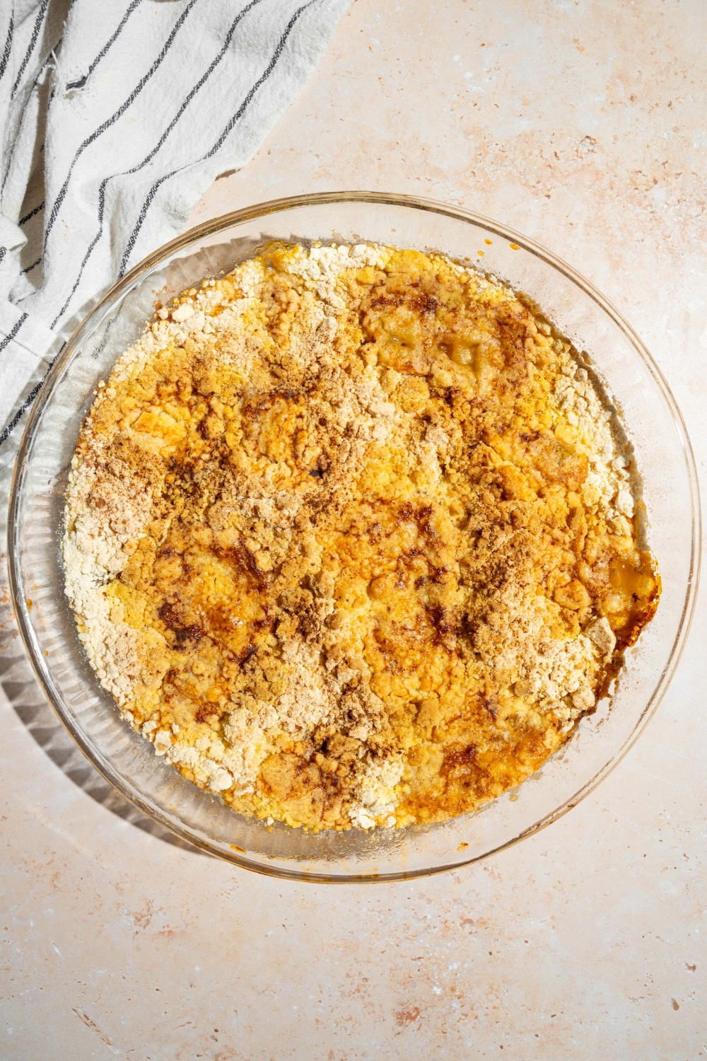 A glass baking dish with baked peach cobbler dump cake. The dish is on a tan counter with a white striped napkin.