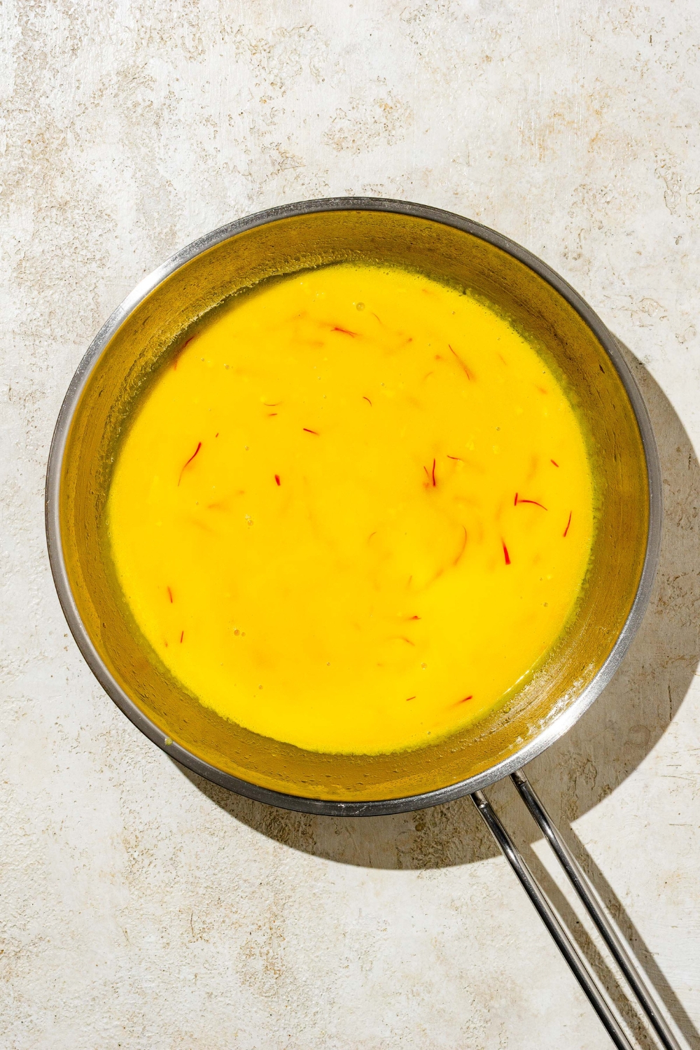 A skillet with creamy saffron sauce. The skillet is on a tan counter.
