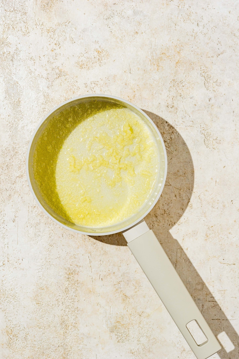 A saucepan with melted butter. The sauce pan is on a tan counter.