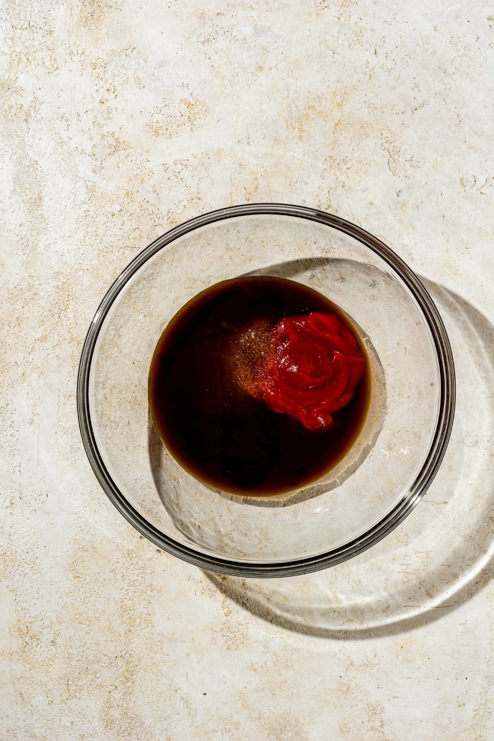 A glass bowl with ingredients to make chicken Katsu sauce. The bowl is on a tan counter.
