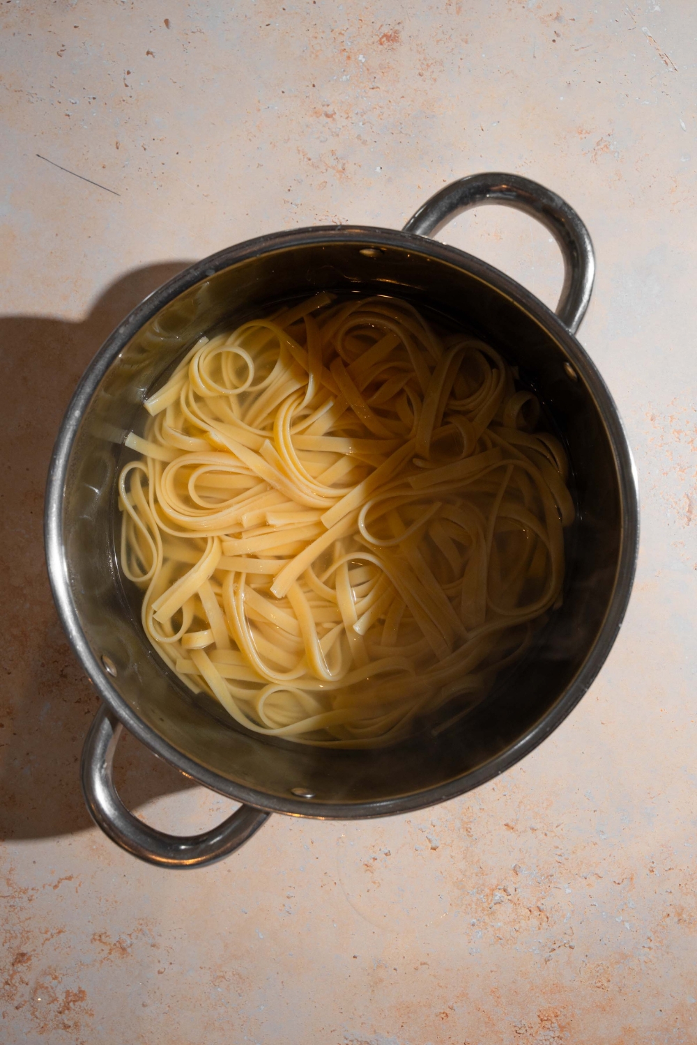 A pot with linguine pasta cooking in water. The pot is on a tan counter.