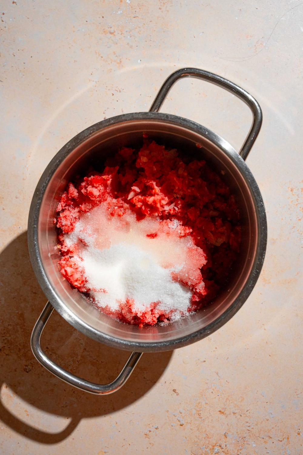 A stock pot with ingredients to make Christmas jam including frozen strawberries, sugar, and lemon juice. The pot is on a tan counter.