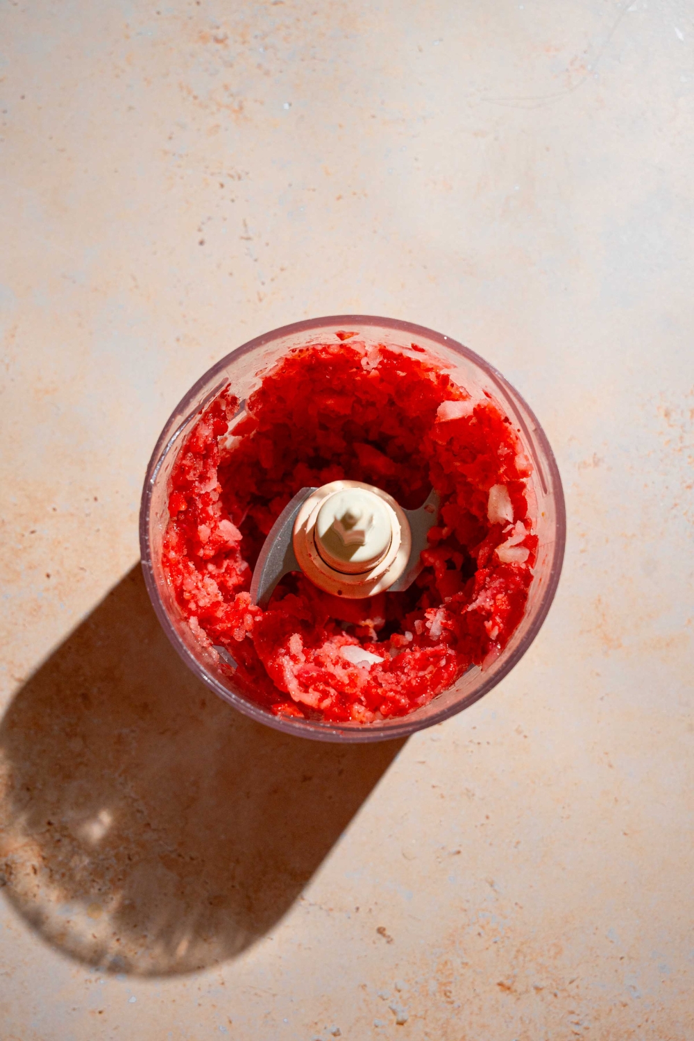 A food processor with mixed frozen strawberries. The food processor is on a tan counter.