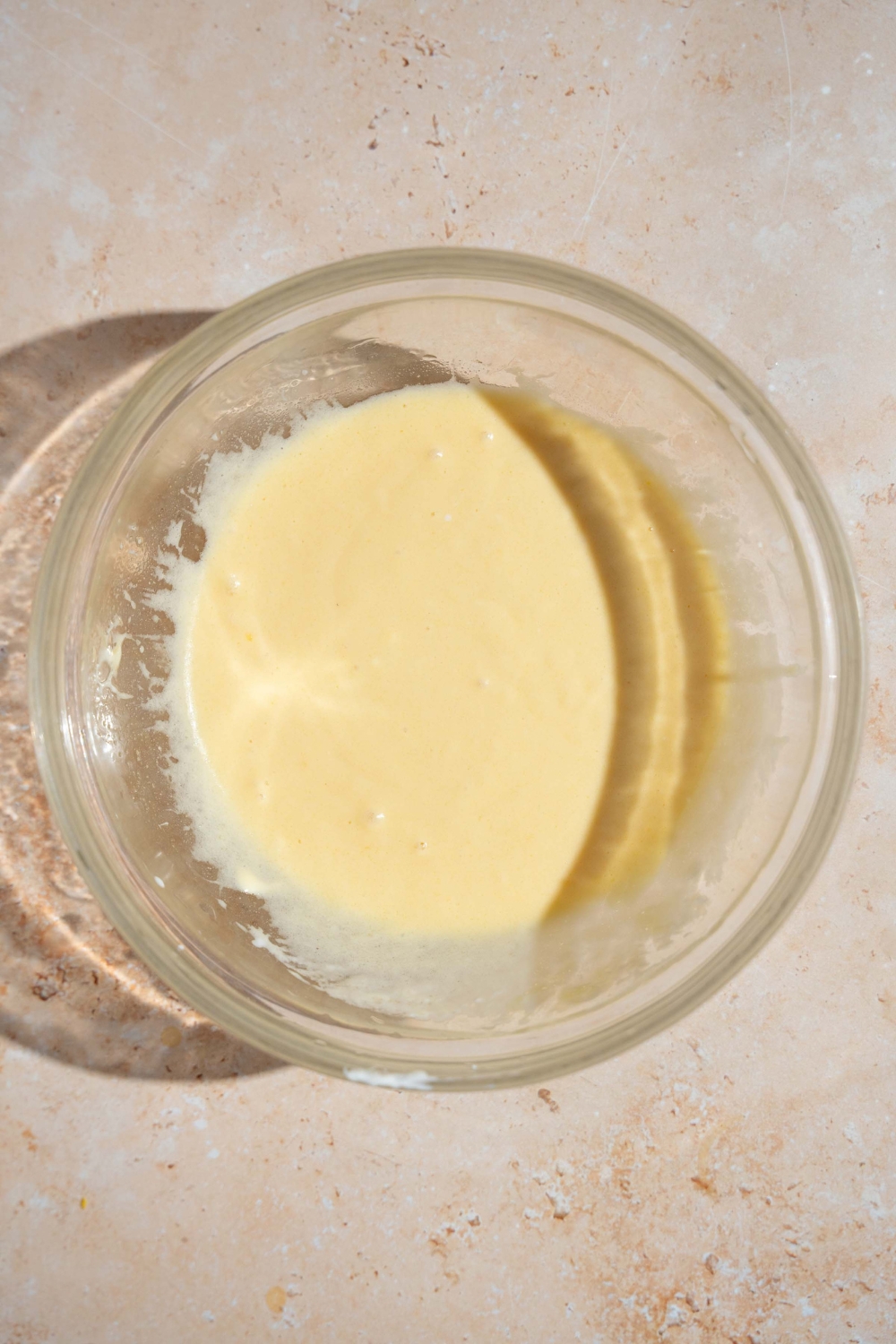 A glass dish with wet ingredients mixed to make copycat Little Bites muffins. The bowl is on a tan counter.