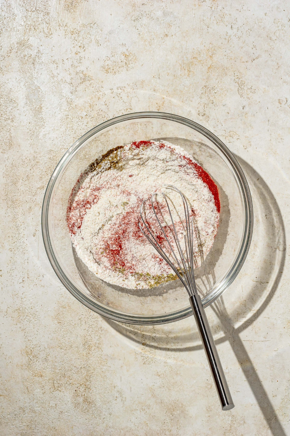 A whisk mixing flour and seasonings for a bloomin onion in a glass bowl.