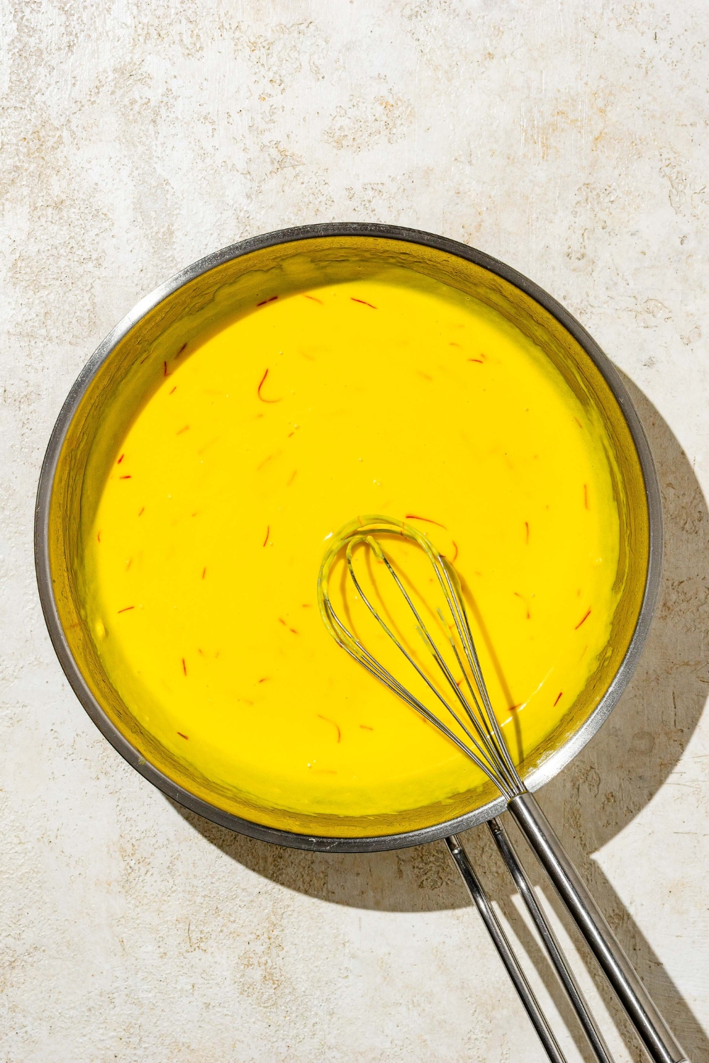 A skillet with a whisk mixing saffron cream sauce. The skillet is on a tan counter.