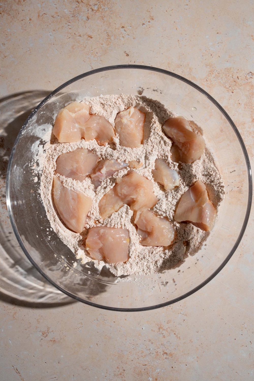 A glass bowl with uncooked chicken nuggets sitting in homemade Chick Fil A seasonings. The bowl is on a tan counter.