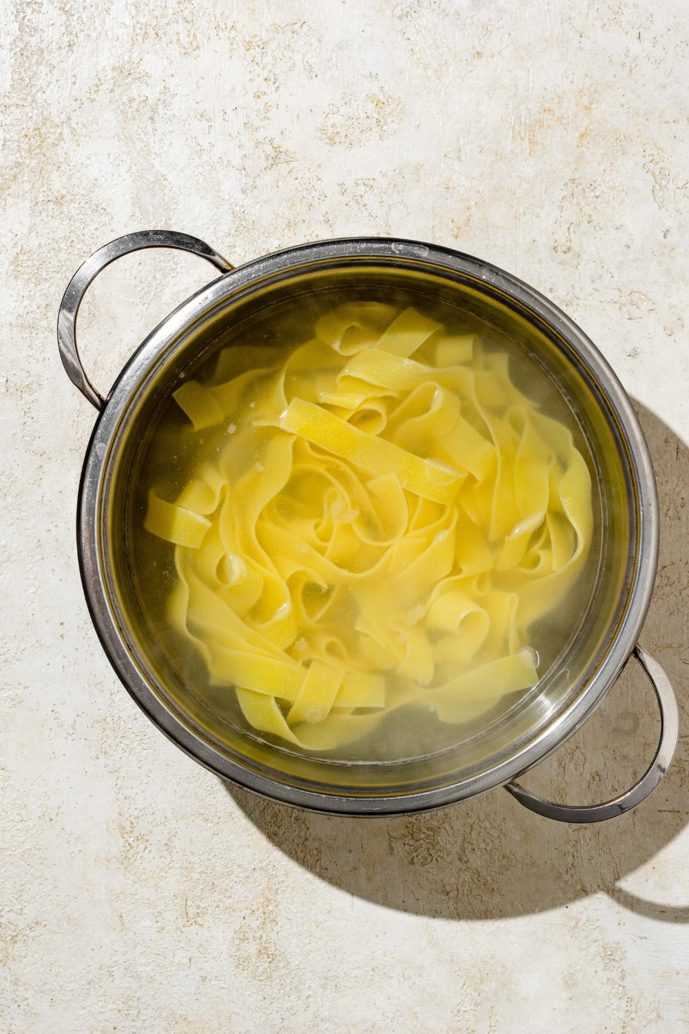 A pot with fettuccine pasta cooking in water. The pot is on a tan counter.