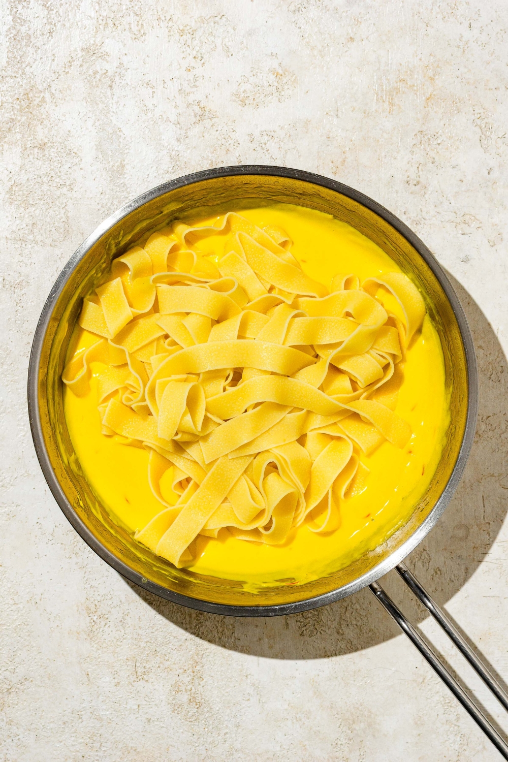 A skillet with fettuccine pasta on top of saffron cream sauce. The skillet is on a tan counter.