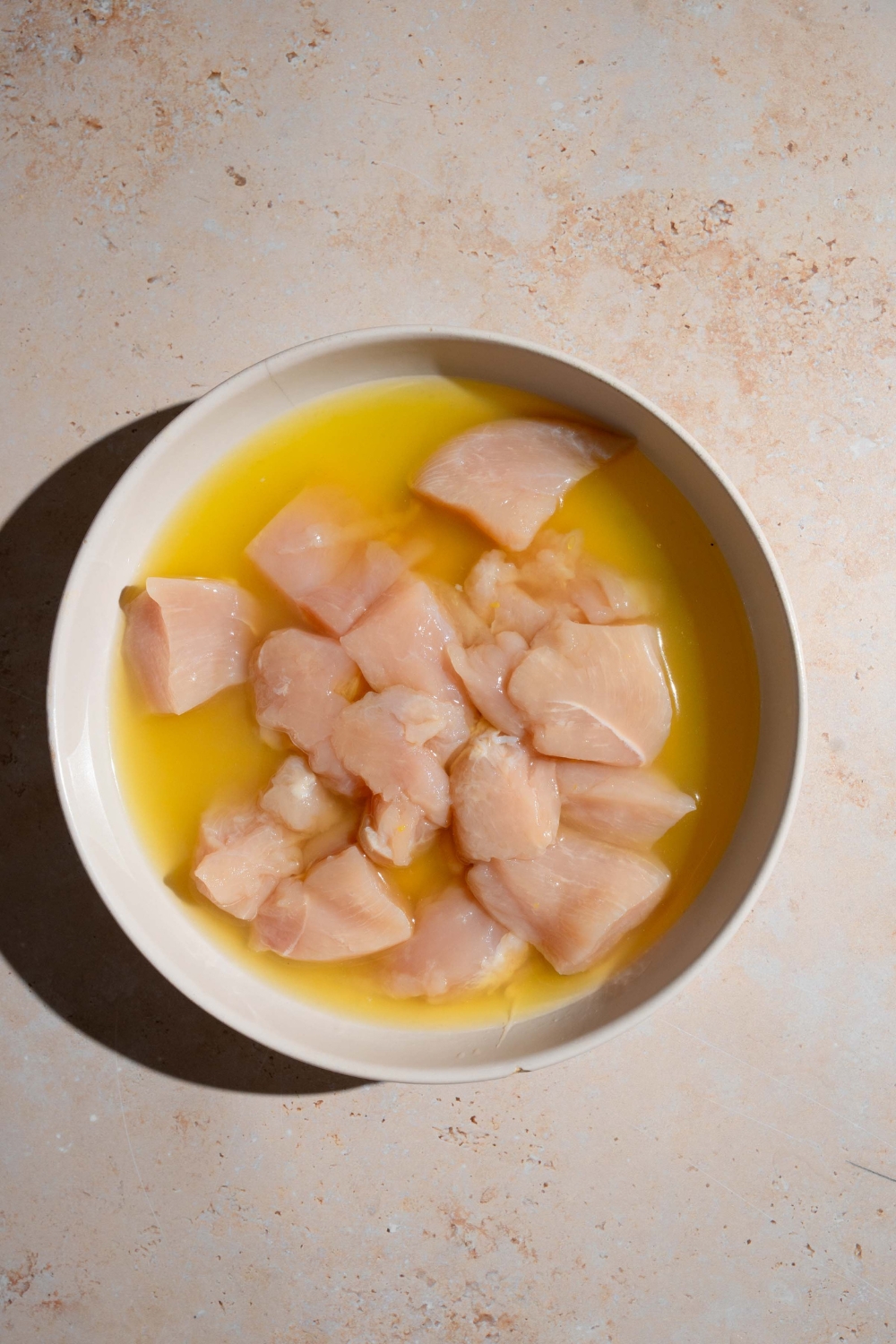 A bowl of uncooked chicken nuggets sitting in marinade. The bowl is on a tan counter.