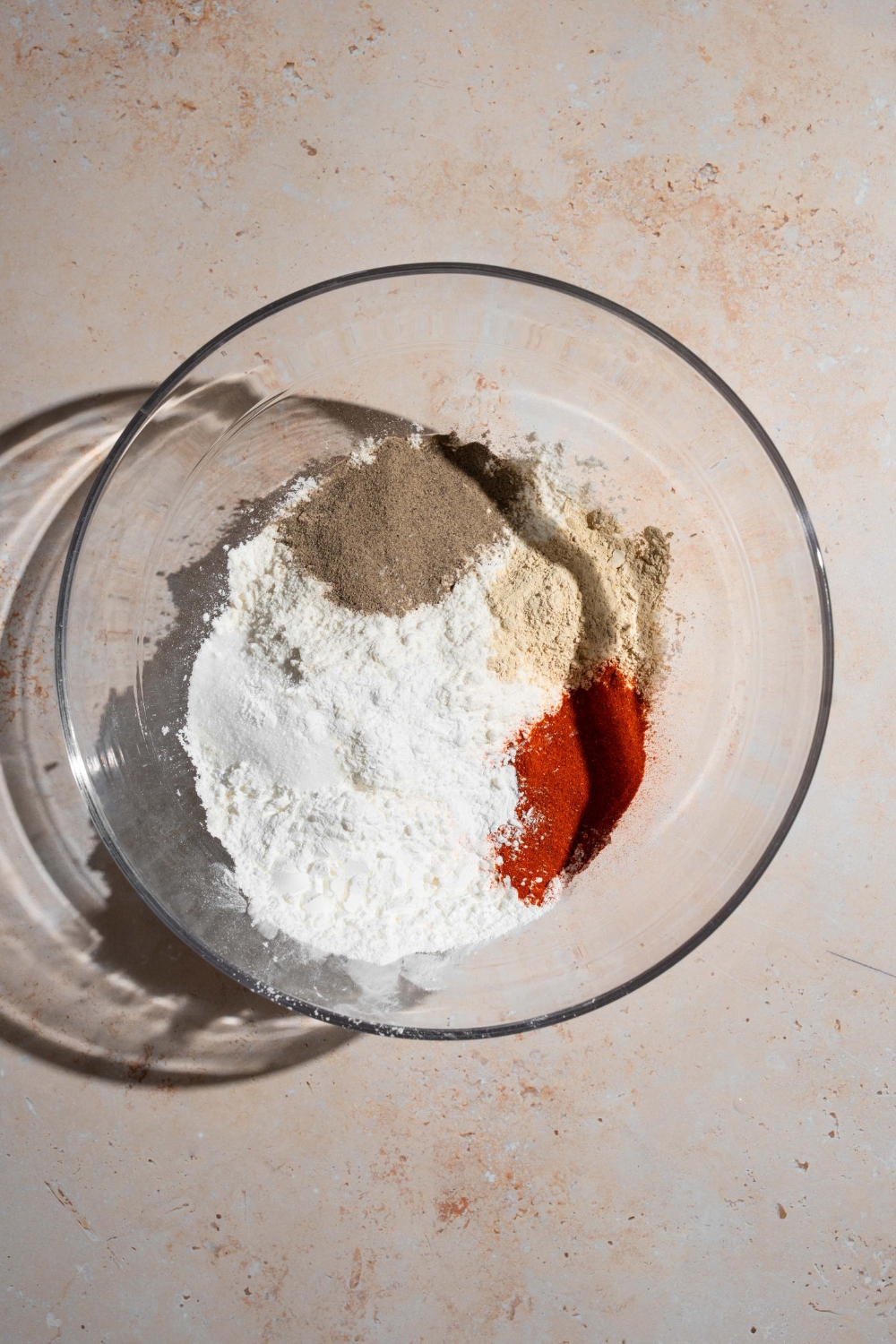 A glass bowl of ingredients for homemade Chick Fil A nuggets including cornstarch, salt, pepper, paprika, and garlic powder. The bowl is on a tan counter.