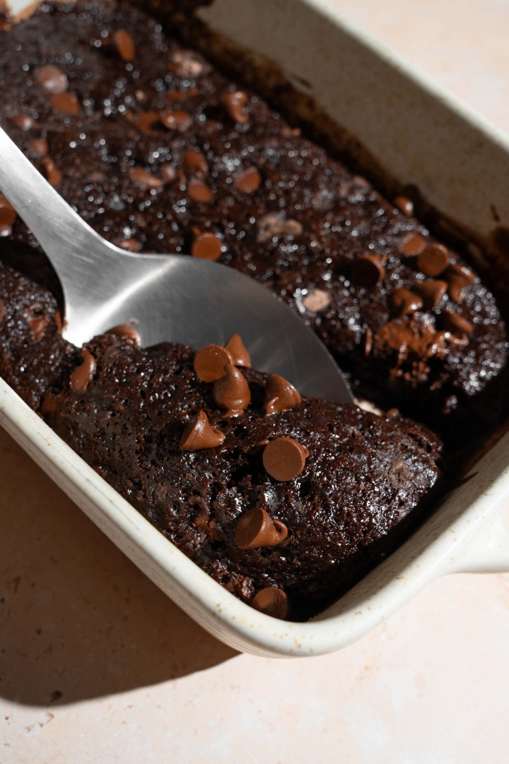 A baking dish with chocolate dump cake. A spoon is taking a bite of cake.