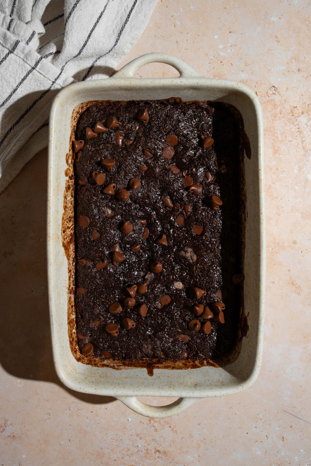 A baking dish with chocolate dump cake batter topped with chocolate chips. The baking dish is on a tan counter.
