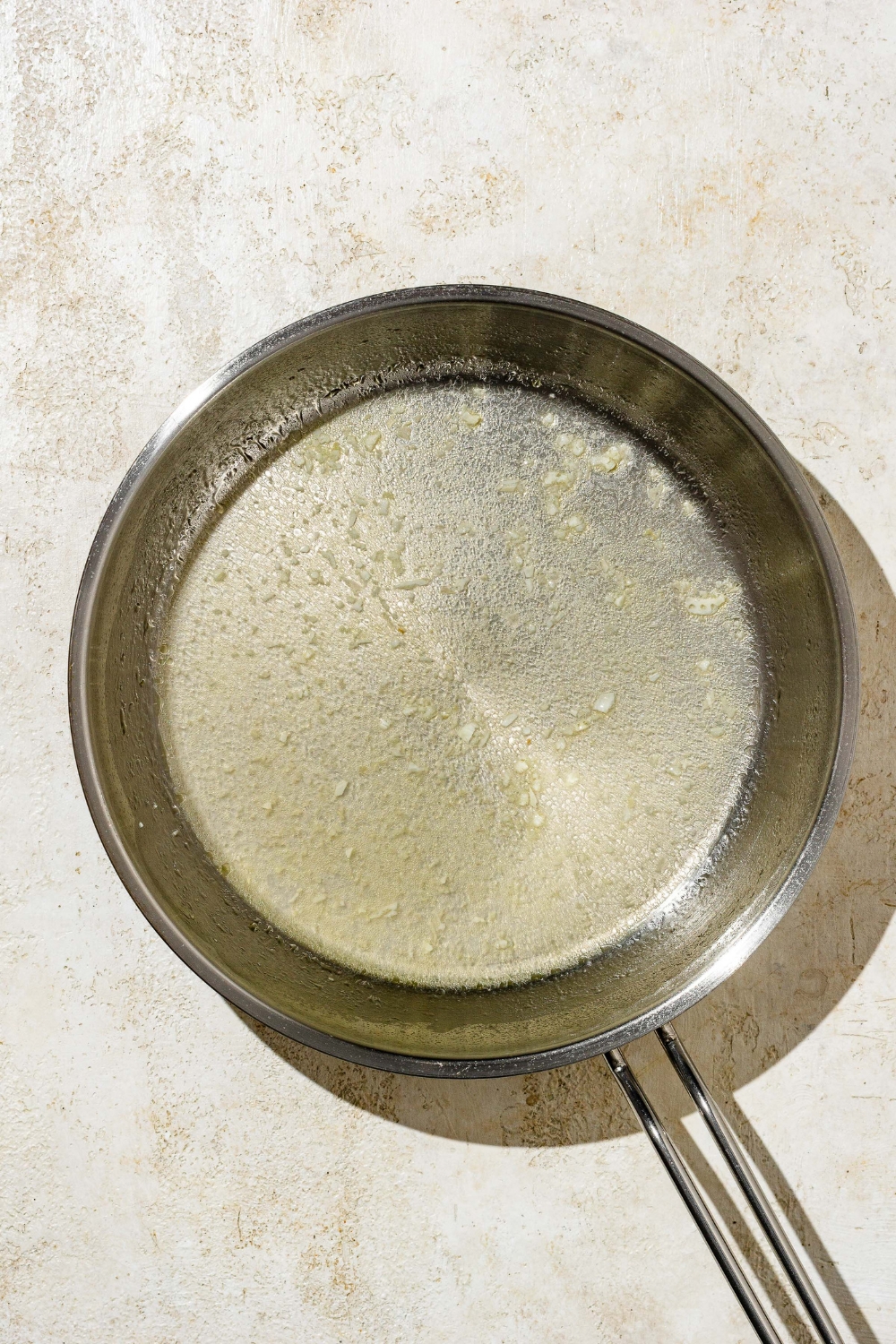 A skillet with garlic sautéing in butter. The skillet is on a tan counter.