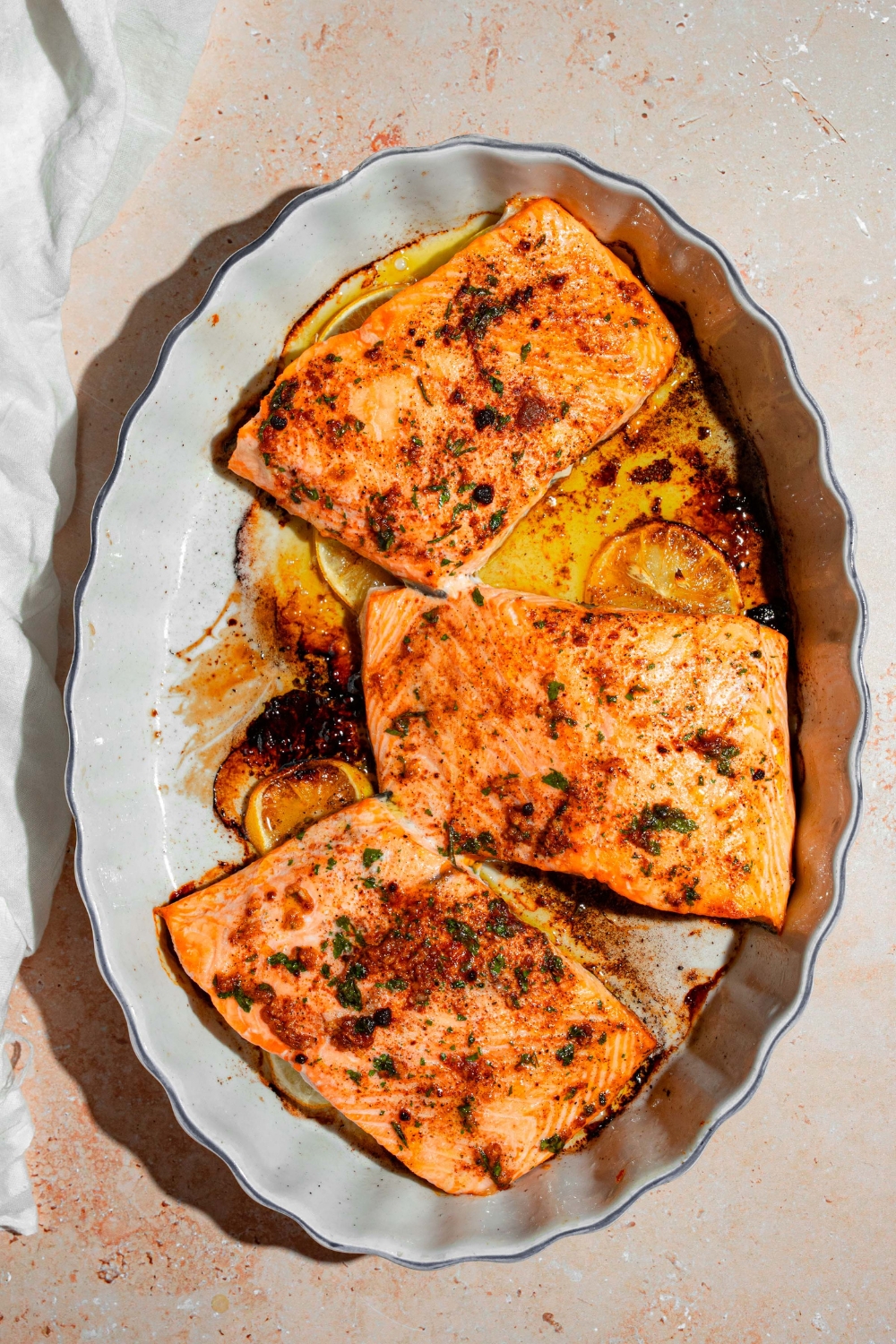 A baking dish with several pieces of baked Sockeye salmon over sliced lemon. The dish is on a tan counter with a white cloth napkin.