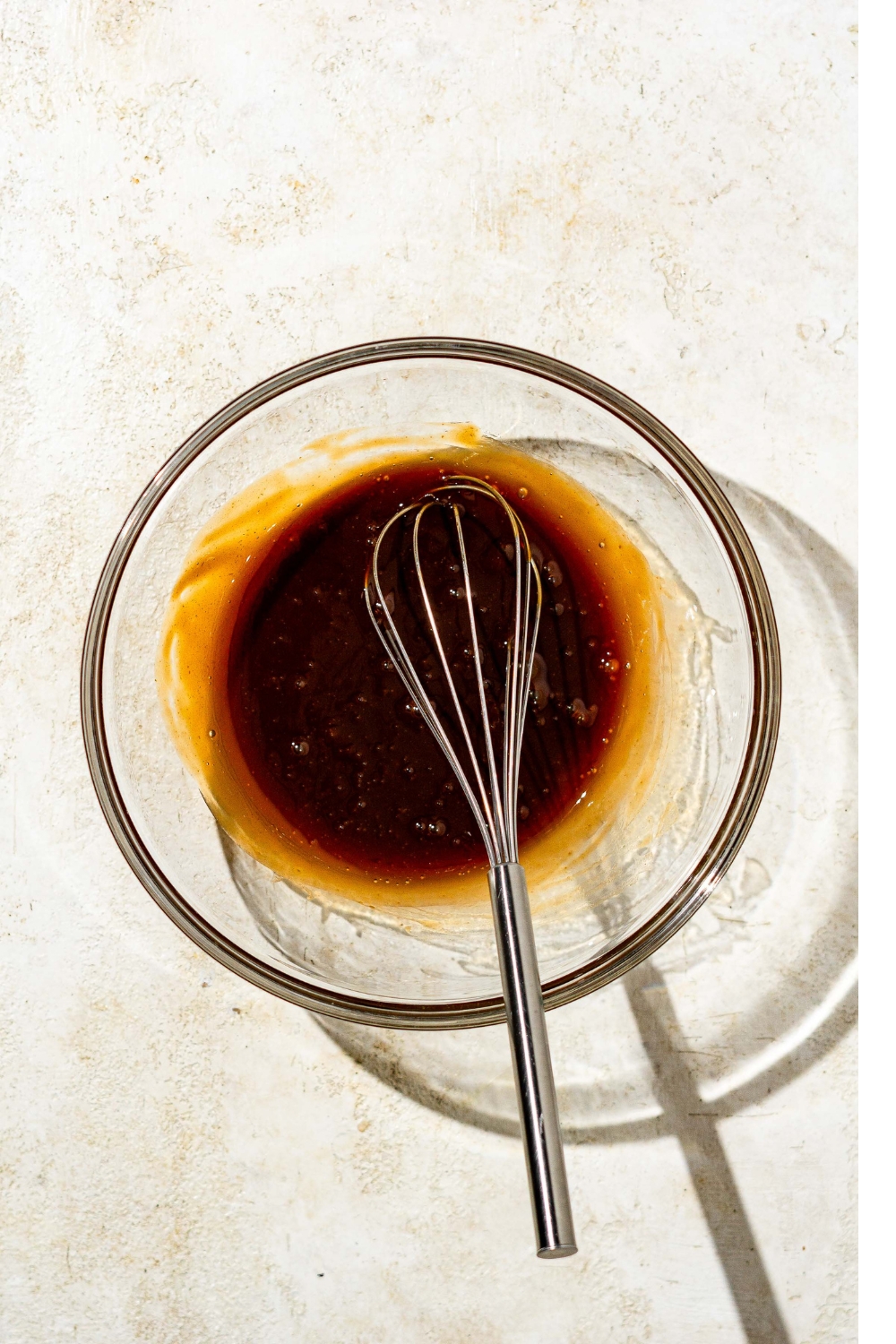 A glass bowl with a whisk mixing chicken Katsu sauce. The bowl is on a tan counter.