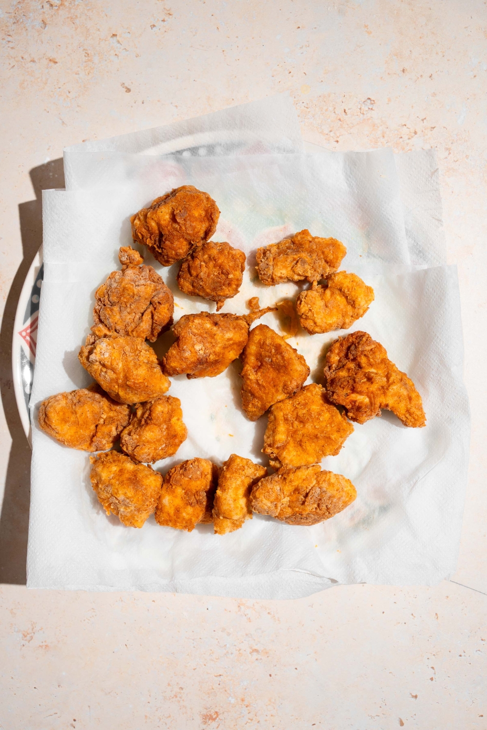A plate lined with parchment paper with fried chicken nuggets. The plate is on a tan counter.