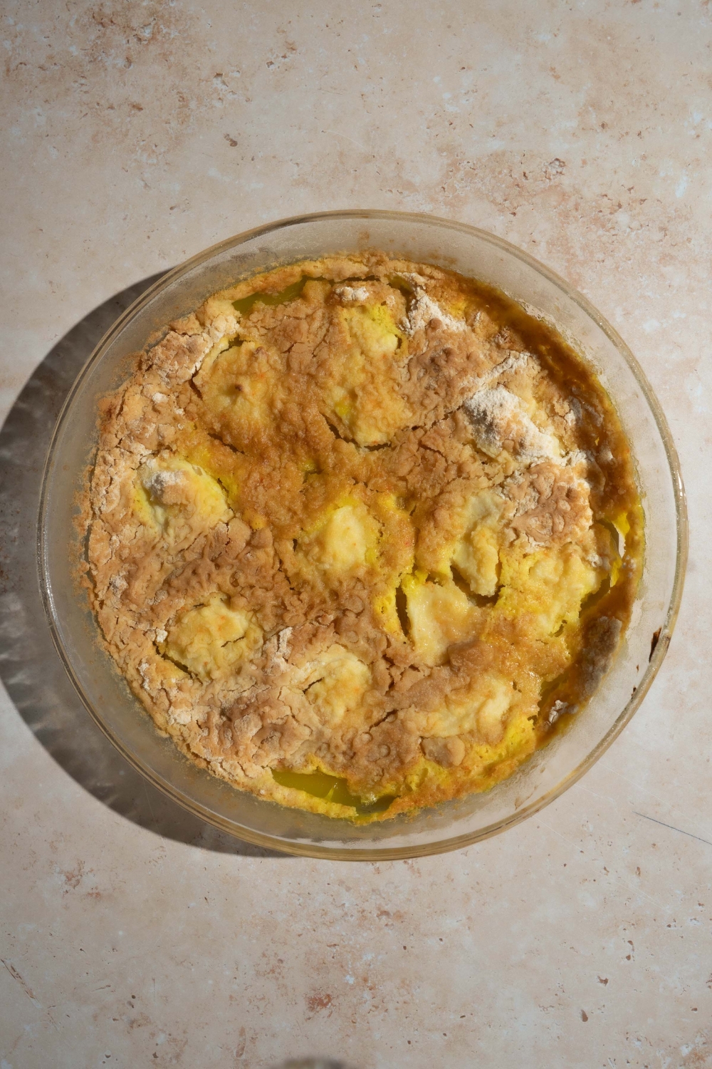 A glass baking dish with baked lemon cream cheese dump cake. The dish is on a tan counter.