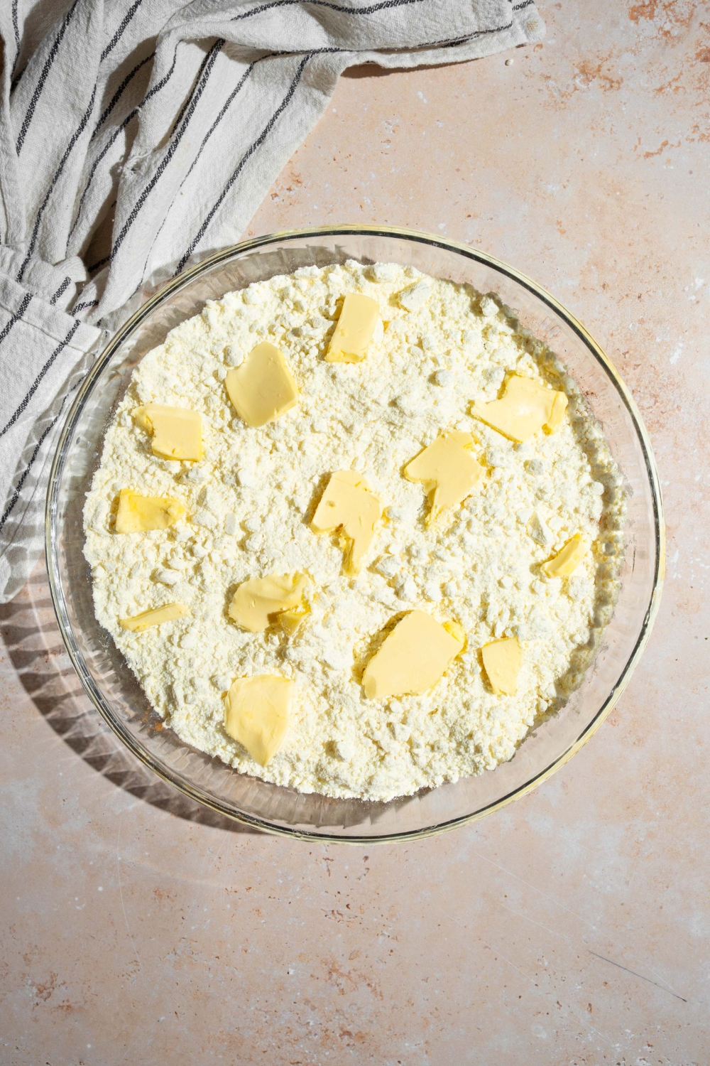 A glass baking dish with canned peaches layered with cake mix and butter on top. The dish is on a tan counter with a white striped napkin.