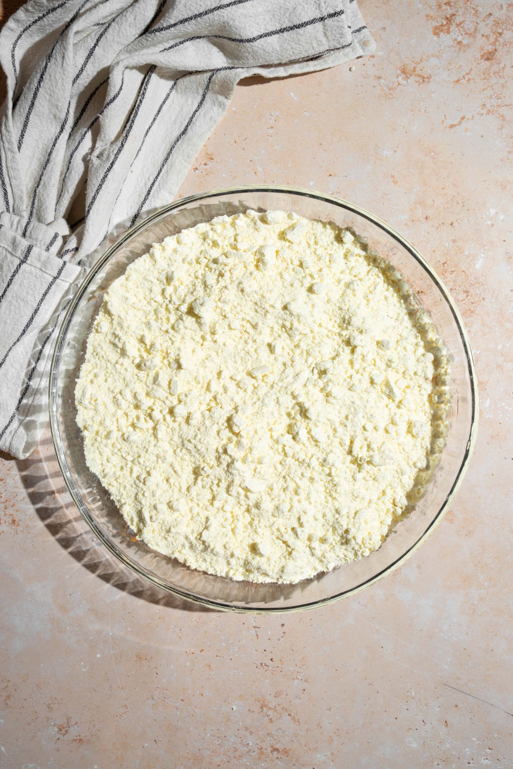 A glass baking dish with canned peaches layered with cake mix. The dish is on a tan counter with a white striped napkin.