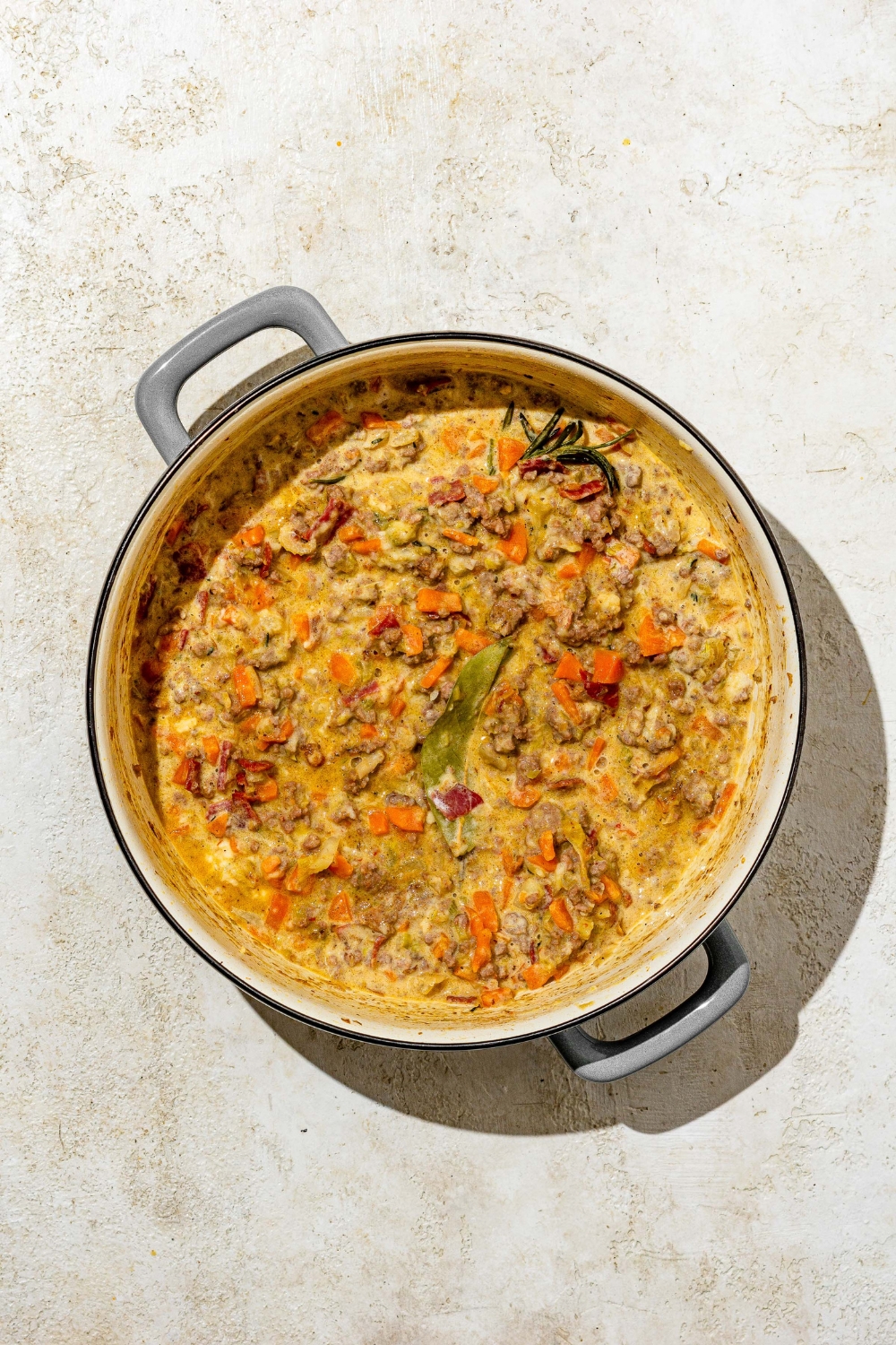 A dutch oven with cooked white bolognese. The pot is on a tan counter.