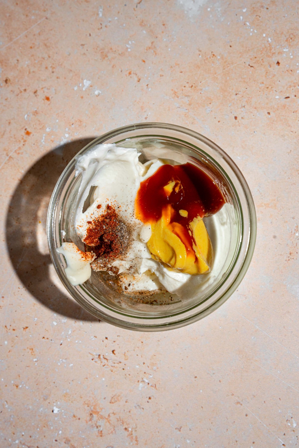 A glass jar with ingredients to make smash burger sauce. The jar is on a tan counter.