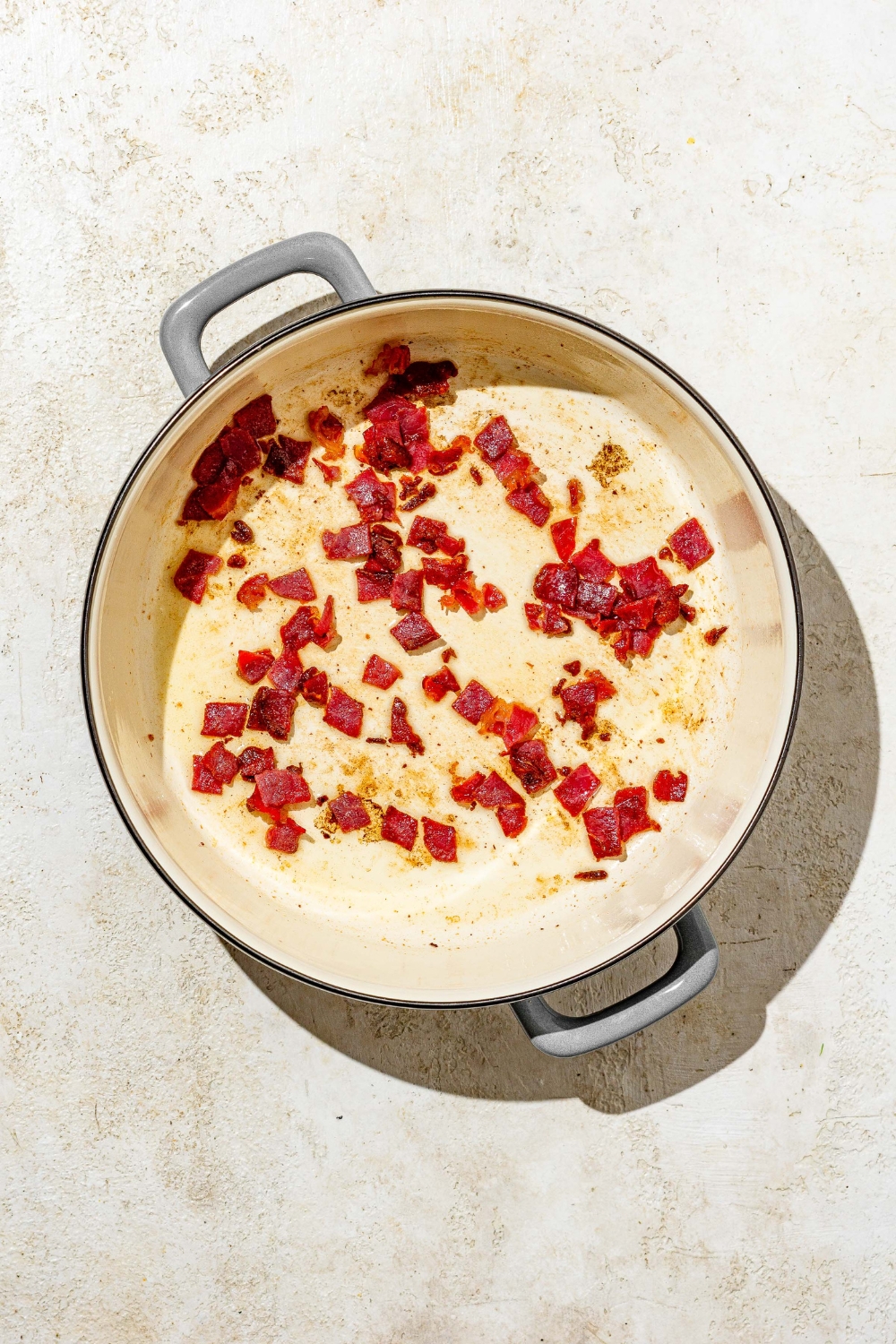 A dutch oven with pancetta cookg in garlic and oil. The pot is on a tan counter.