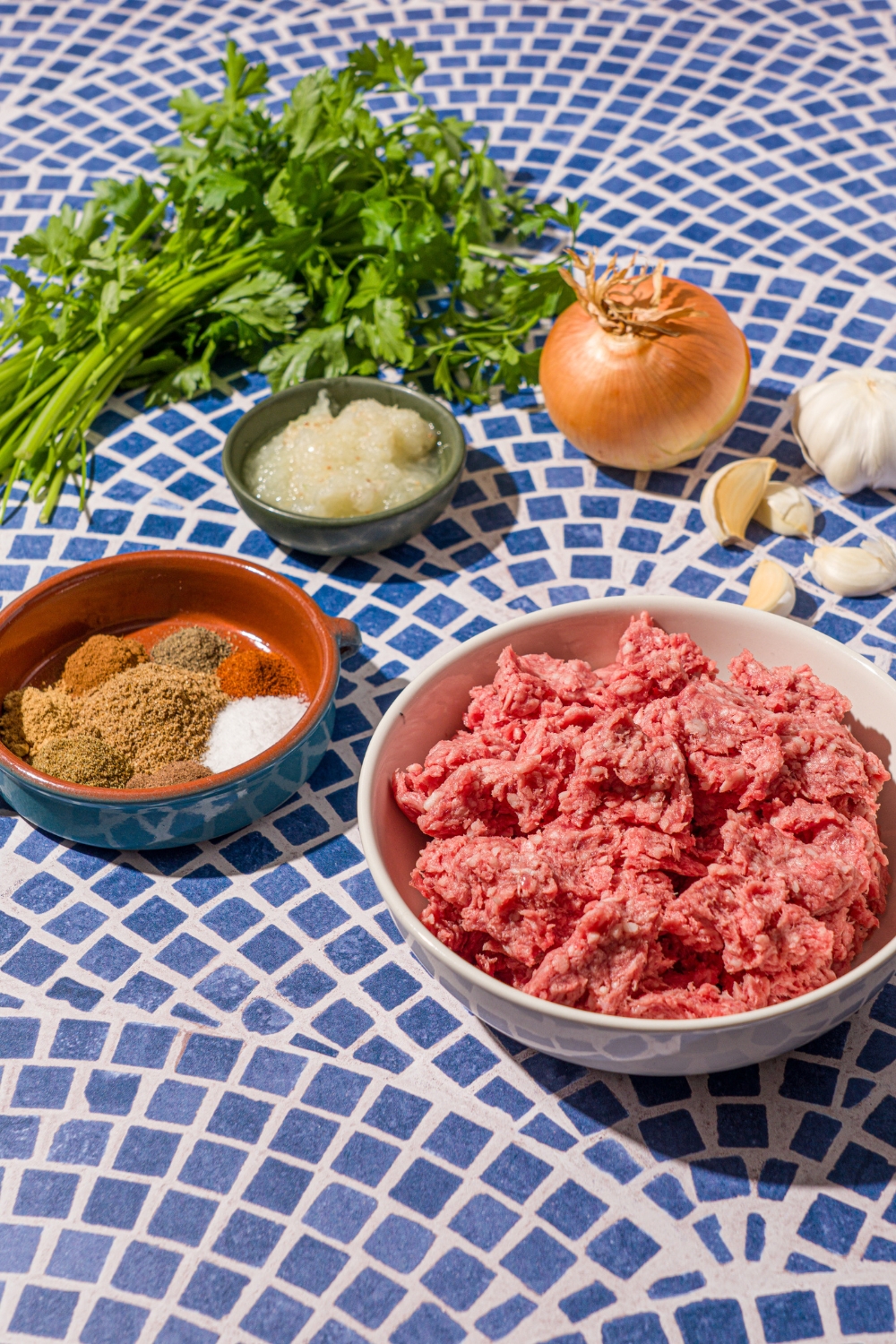 Small bowls of ingredients to make Kafta kabobs including ground lamb, garlic, onion, fresh parsley, and seasonings.