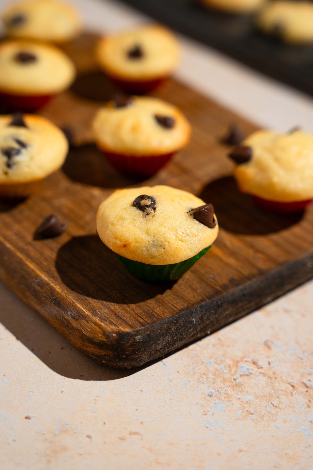 A wooden board with copycat Little Bites chocolate chip muffins. The board is garnished with chocolate chips. The board is on a tan counter.