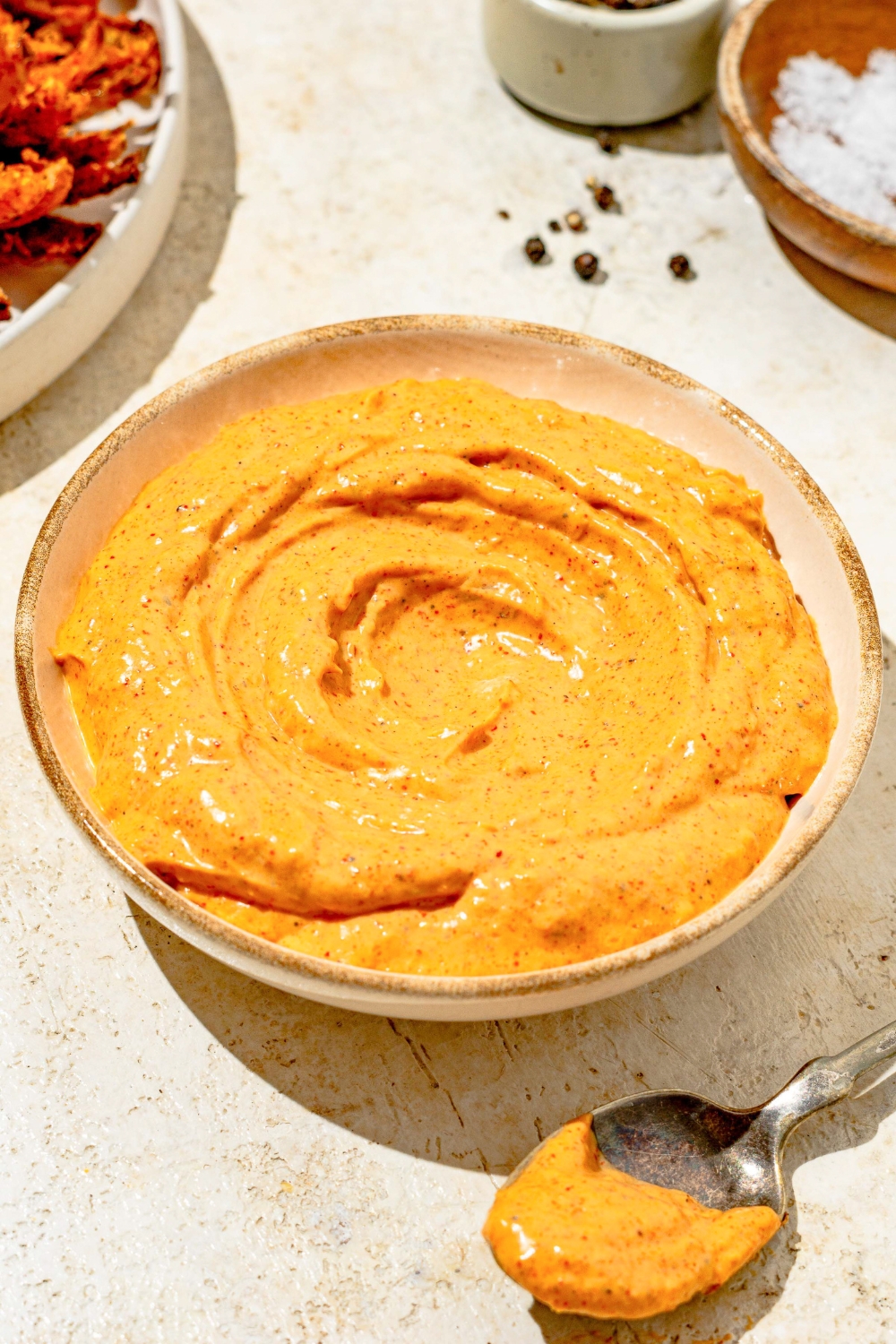 A bowl of copycat Outback bloomin onion sauce on a tan counter with a spoon coated in the sauce.