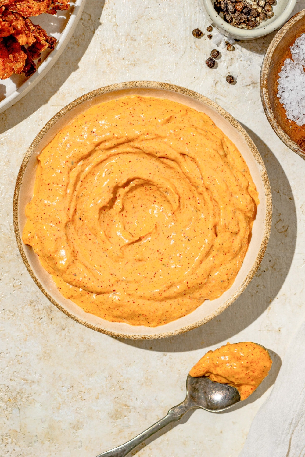 A bowl of copycat Outback bloomin onion sauce on a tan counter with a spoon coated in the sauce.