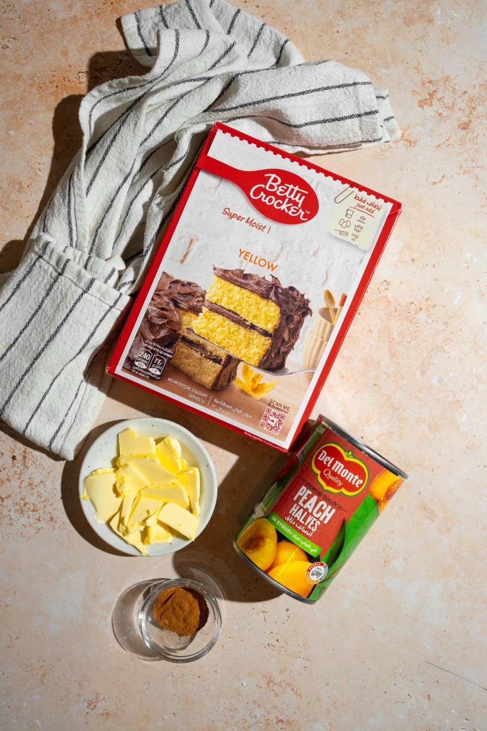 An overhead shot of several ingredients for peach cobbler dump cake including canned peaches, cake mix, cinnamon, and butter.
